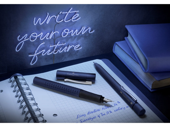 Lifestyle image featuring the Faber-Castell Grip 2011 writing collection in Classic Blue, including a fountain pen, ballpoint pen and Grip 2001 graphite pencil displayed beside handwritten notes, books and a notebook, highlighting the ergonomic Grip dot design, coordinated blue finish and smooth everyday writing performance for studying, journaling and professional writing.