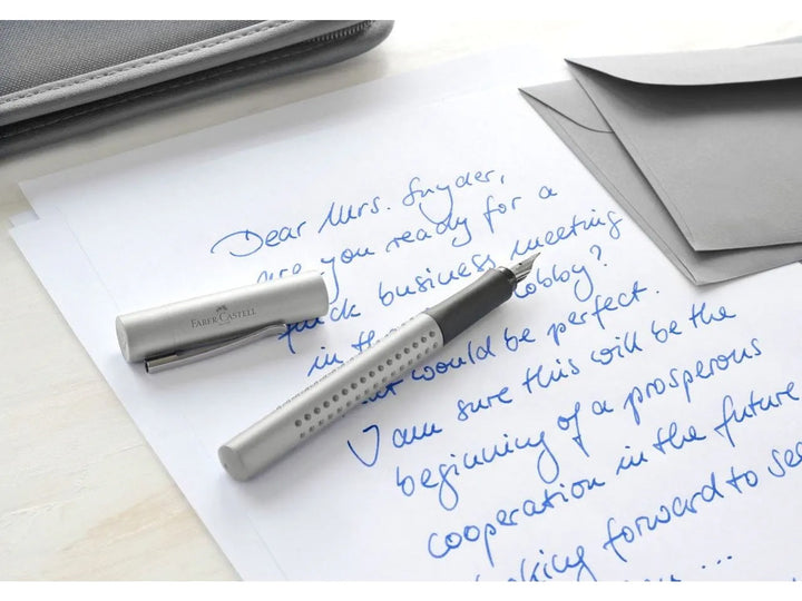 Faber-Castell Grip 2011 Fountain Pen in Silver shown beside a handwritten letter and envelopes, featuring an ergonomic triangular barrel with patented Grip dots, durable stainless steel nib and metal pocket clip for everyday handwriting, journaling, note-taking and professional correspondence.