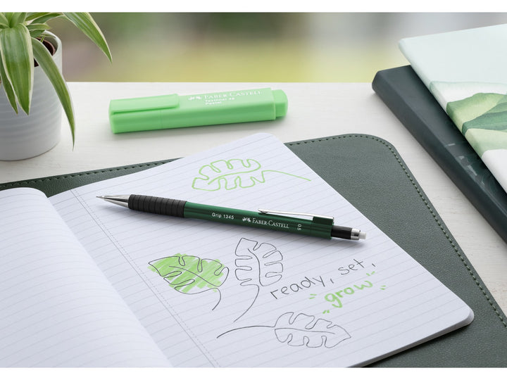 Faber-Castell Grip 1345 Mechanical Pencil 0.5mm in Green shown on an open notebook with botanical sketches and notes, featuring a cushioned lead sleeve to reduce breakage, non-slip rubber grip zone, retractable lead mechanism and extra-long twist-out eraser for writing, sketching, journaling and study.