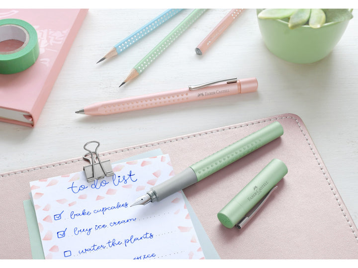 Lifestyle image featuring the Faber-Castell Grip Pearl Edition writing collection in Mint, including a fountain pen, ballpoint pen and matching graphite pencils displayed beside a handwritten to-do list, notebook, washi tape and potted succulent, highlighting the pearlescent mint finish, ergonomic Grip dot design and coordinated stationery range for journaling, planning, studying and everyday writing.