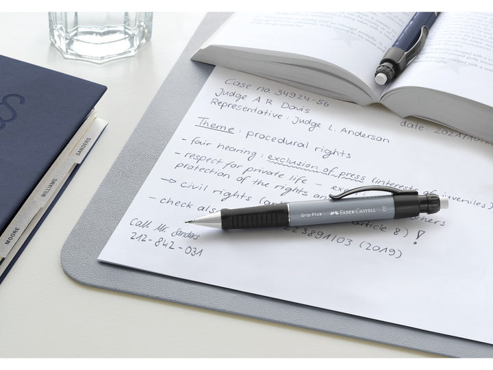 Faber-Castell Grip Plus Mechanical Pencil 0.7mm in Stone Grey resting on handwritten notes beside an open book, demonstrating the ergonomic soft-grip zone, retractable lead sleeve, integrated eraser and comfortable design for studying, note-taking, technical drawing and everyday writing.