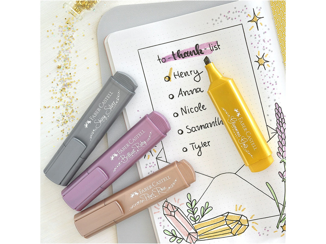Faber-Castell Textliner 46 Metallic Highlighters in Shiny Silver, Brilliant Ruby, Pearl Rose and Glamorous Gold displayed beside a decorated bullet journal page, demonstrating shimmering metallic ink effects, chisel-tip highlighting and creative hand lettering for journaling, planners, colour-coding and craft projects on light and dark paper.