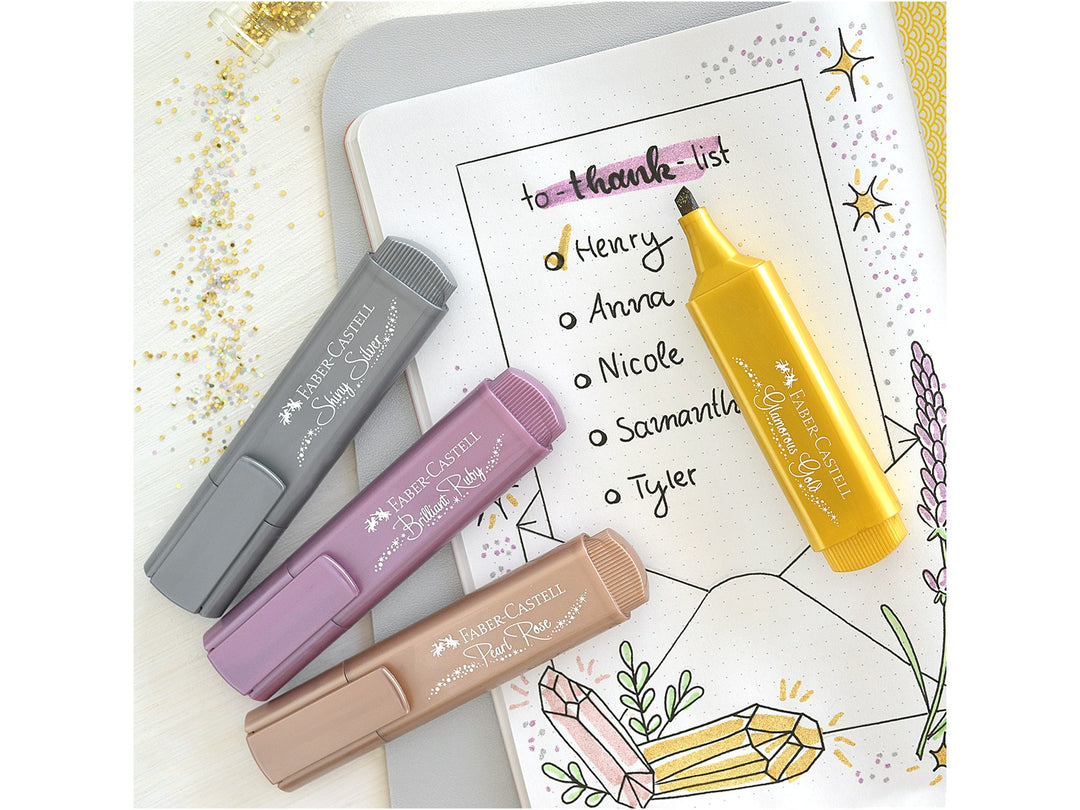 Faber-Castell Textliner 46 Metallic Highlighters in Shiny Silver, Brilliant Ruby, Pearl Rose and Glamorous Gold displayed beside a decorated bullet journal page, demonstrating shimmering metallic ink effects, chisel-tip highlighting and creative hand lettering for journaling, planners, colour-coding and craft projects on light and dark paper.