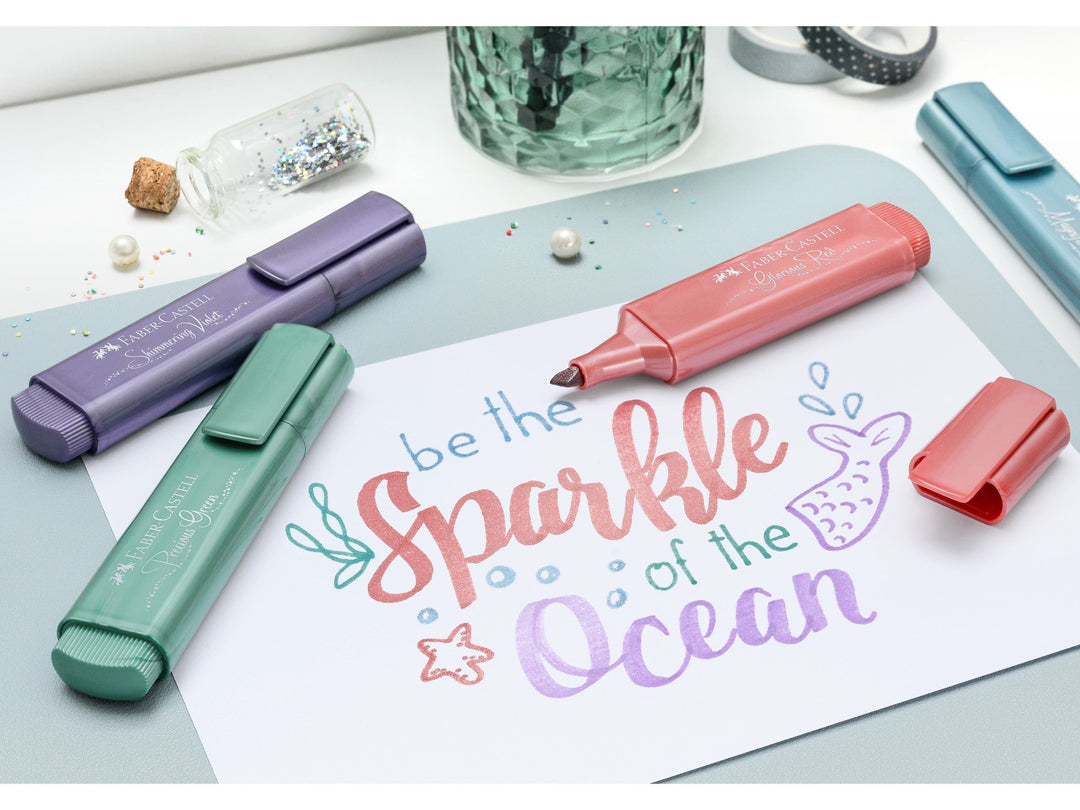 Faber-Castell Textliner 46 Metallic Highlighters being used to create decorative hand lettering and artwork, featuring metallic highlighters in red, violet, green and blue shades with shimmering metallic ink effects on light paper for journaling, card making and creative projects.