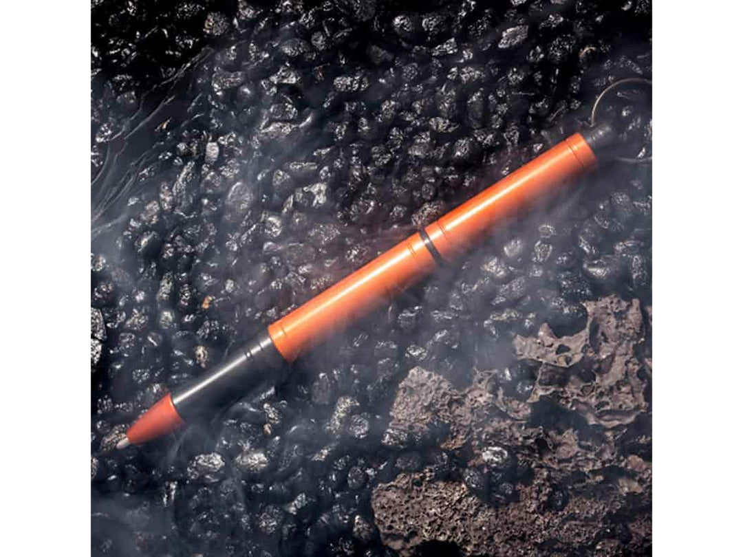 Fisher Space Pen Backpacker orange pen on rugged textured surface with mist effect showing outdoor durability