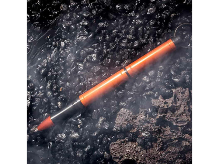 Fisher Space Pen Backpacker orange pen on rugged textured surface with mist effect showing outdoor durability