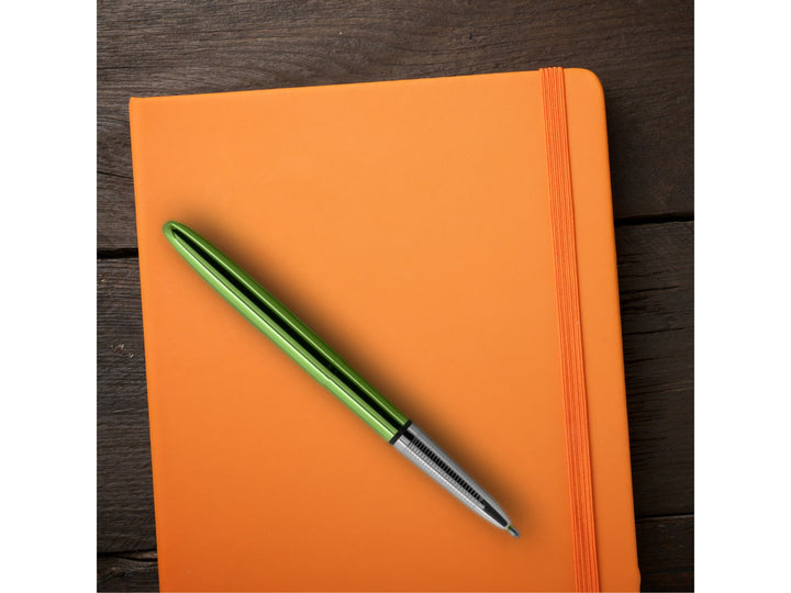 Fisher Space Pen Bullet Aurora Borealis lime green pen placed on orange notebook showing lifestyle use