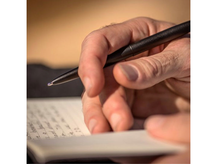 Fisher Space Pen Bullet black pen held in hand while writing in notebook showing everyday use