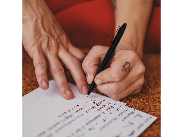 Fisher Space Pen Bullet black pen with clip held in hand writing on grid paper showing everyday use