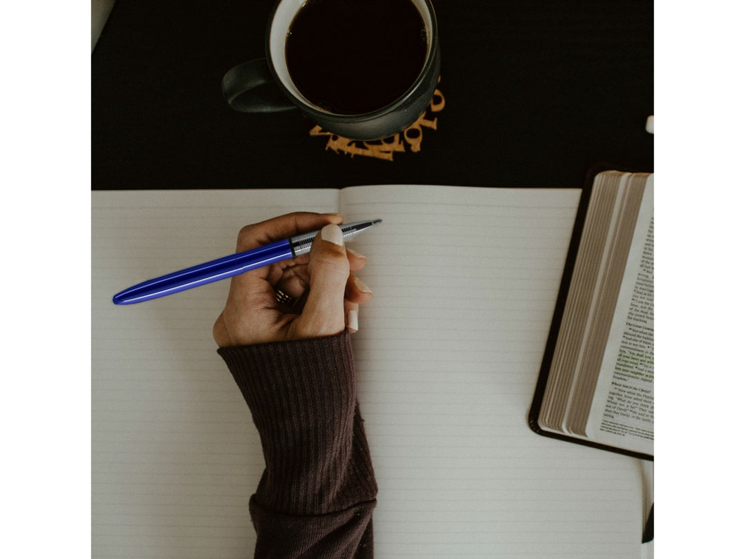 Fisher Space Pen Bullet Blue Moon Blueberry pen used for writing in notebook with coffee cup lifestyle setting
