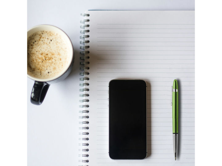 Fisher Space Pen Bullet Aurora Borealis lime green pen with clip placed on notebook alongside smartphone and coffee cup