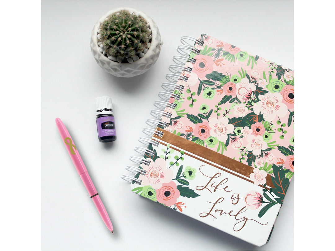 Fisher Space Pen Bullet pink Breast Cancer Awareness pen with ribbon symbol placed beside floral notebook and small plant