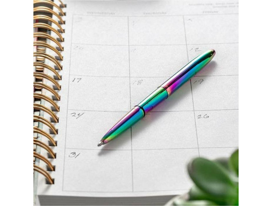Fisher Space Pen Bullet rainbow pen placed on monthly planner notebook showing iridescent colour shift finish