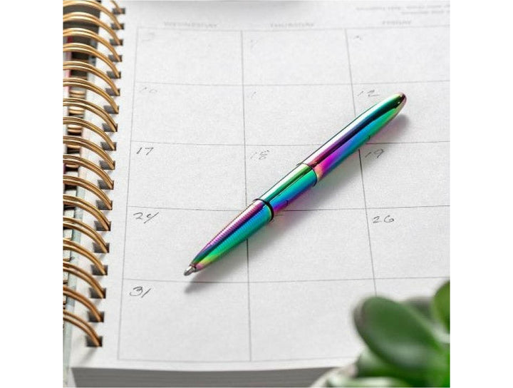 Fisher Space Pen Bullet rainbow pen placed on monthly planner notebook showing iridescent colour shift finish