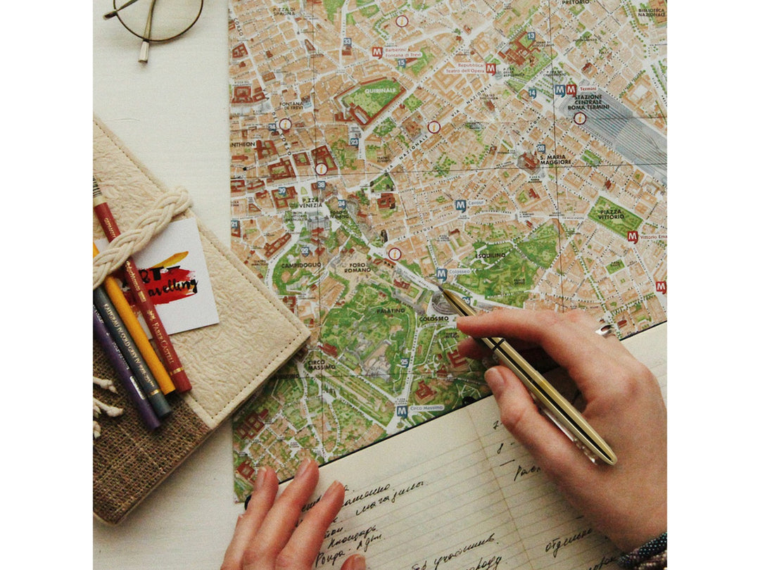Fisher Space Pen Bullet raw brass pen held over travel map and notebook showing everyday carry and navigation use