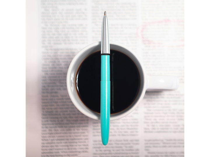 Fisher Space Pen Bullet Tahitian Blue pen placed over coffee cup on open book showing lifestyle use