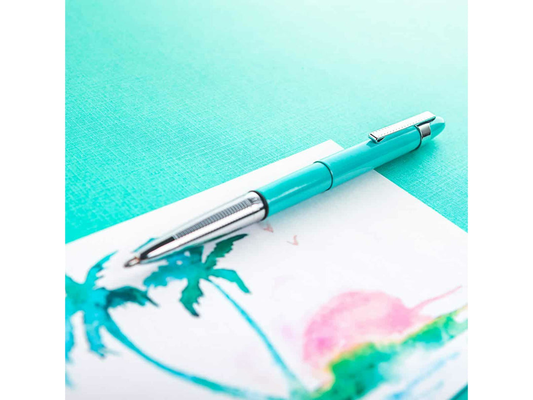 Fisher Space Pen Bullet Tahitian Blue ballpoint pen placed on surface next to watercolour artwork