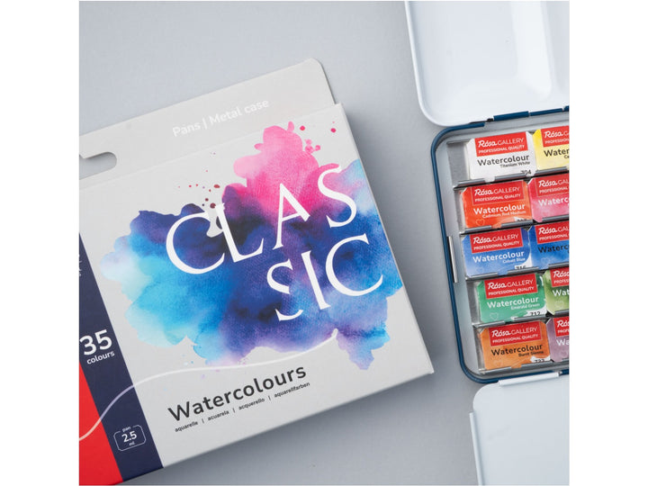 Close-up of the ROSA Gallery Classic Watercolour Set featuring updated Classic Collection packaging alongside an open metal watercolour case filled with 35 professional watercolour half pans. The image highlights the extensive colour selection, integrated mixing palette and versatile artist palette designed for watercolour painting, sketching and illustration