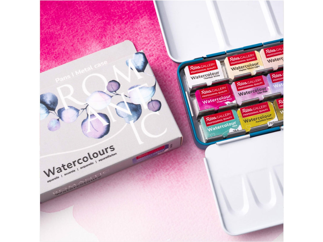 Lifestyle image of the ROSA Gallery Romantic Watercolour Set featuring updated Romantic Collection packaging alongside an open metal watercolour case filled with 21 professional watercolour half pans. The image showcases soft pink washes, integrated mixing palette surfaces and a curated colour palette developed for floral painting, botanical artwork, illustration and expressive watercolour techniques