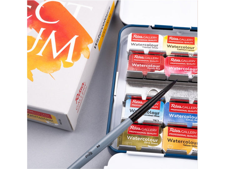 Close-up of the ROSA Gallery Spectrum Watercolour Set featuring an included travel brush resting across professional watercolour half pans inside a metal case, alongside updated Spectrum Collection packaging. The image highlights the vibrant colour selection, metal pan layout and portable design for watercolour painting, illustration and creative colour mixing