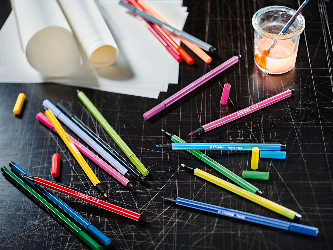 Assorted STABILO Pen 68 felt-tip pens in a variety of bright colours displayed uncapped on a creative workspace with drawing paper and art supplies