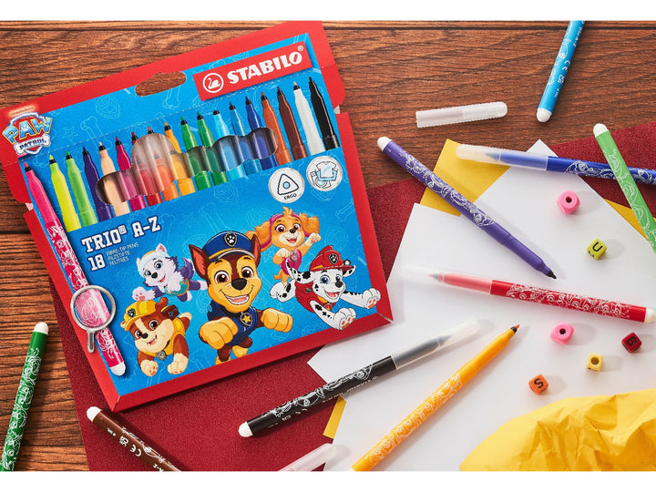 STABILO Trio A-Z PAW Patrol Wallet of 18 felt-tip pens displayed on a wooden craft desk with assorted colourful pens, paper and creative accessories