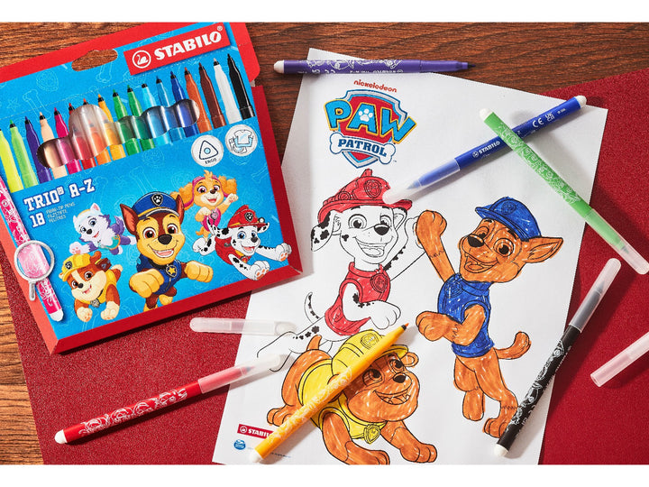 STABILO Trio A-Z PAW Patrol Wallet of 18 felt-tip pens displayed beside a PAW Patrol colouring sheet with assorted colourful pens on a wooden craft desk