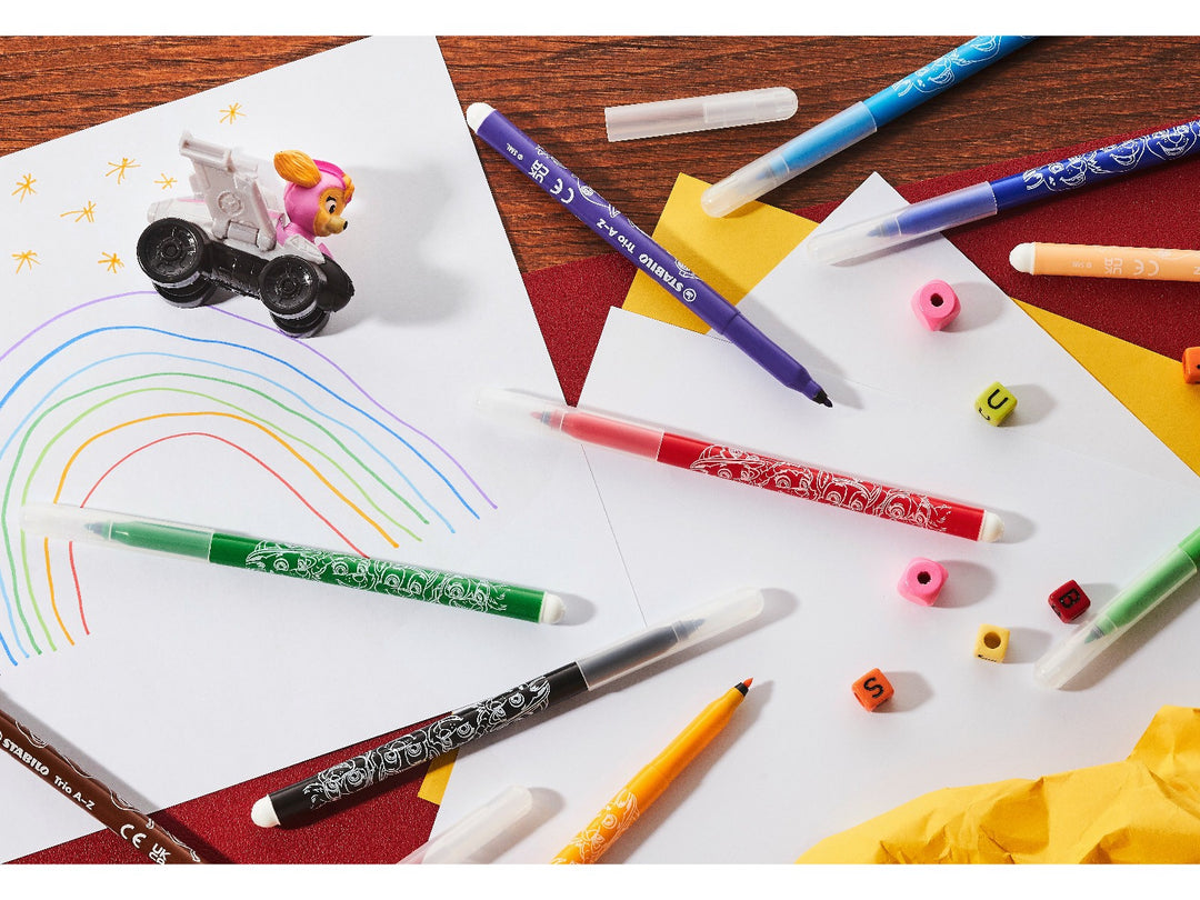STABILO Trio A-Z PAW Patrol felt-tip pens in assorted colours displayed across a creative desk with a rainbow drawing, paper, PAW Patrol toy and colourful craft accessories