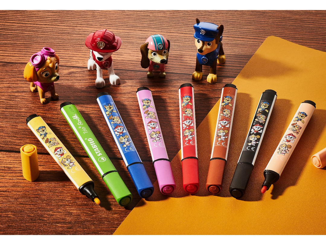 Eight STABILO Trio Scribbi PAW Patrol felt-tip pens in assorted colours displayed with PAW Patrol character figures on a wooden desk