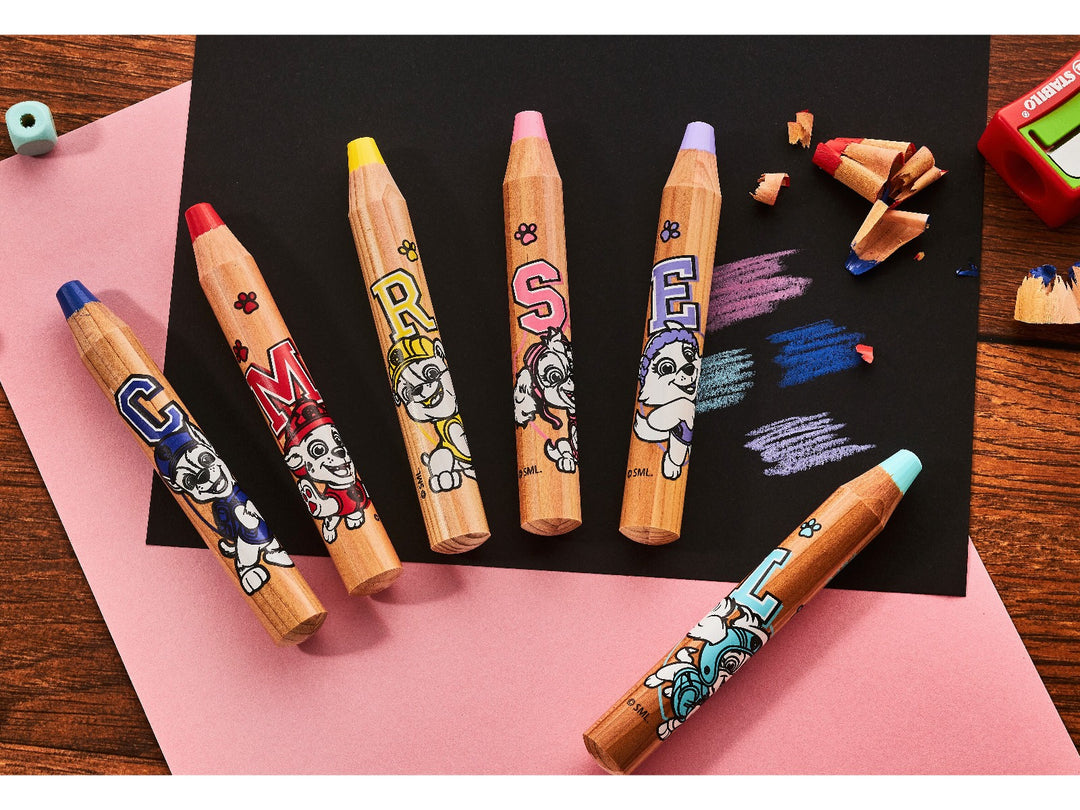 Six STABILO woody 3 in 1 PAW Patrol chunky coloured pencils in assorted colours displayed on black paper with colourful pencil strokes, shavings and a sharpener