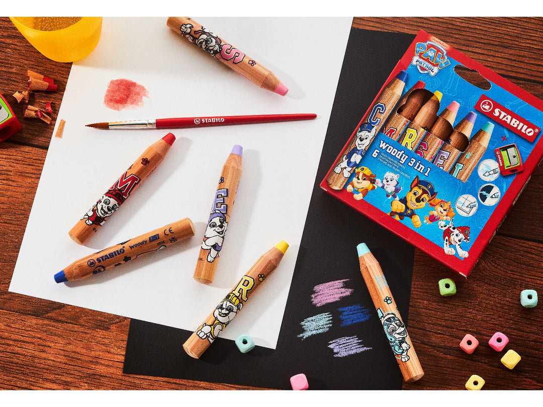 STABILO woody 3 in 1 PAW Patrol coloured pencils displayed with the Wallet of 6, watercolour brush, colour swatches on white and black paper, pencil shavings and sharpener