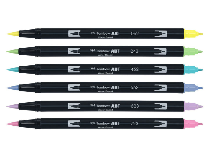 Tombow ABT Dual Brush Pen Pastel Colours Set of 6 displayed individually, featuring Pale Yellow (062), Mint (243), Process Blue (452), Mist Purple (553), Purple Sage (623) and Pink (723), each with dual brush and fine tips visible for hand lettering, colouring, journaling, illustration and watercolour-style effects.