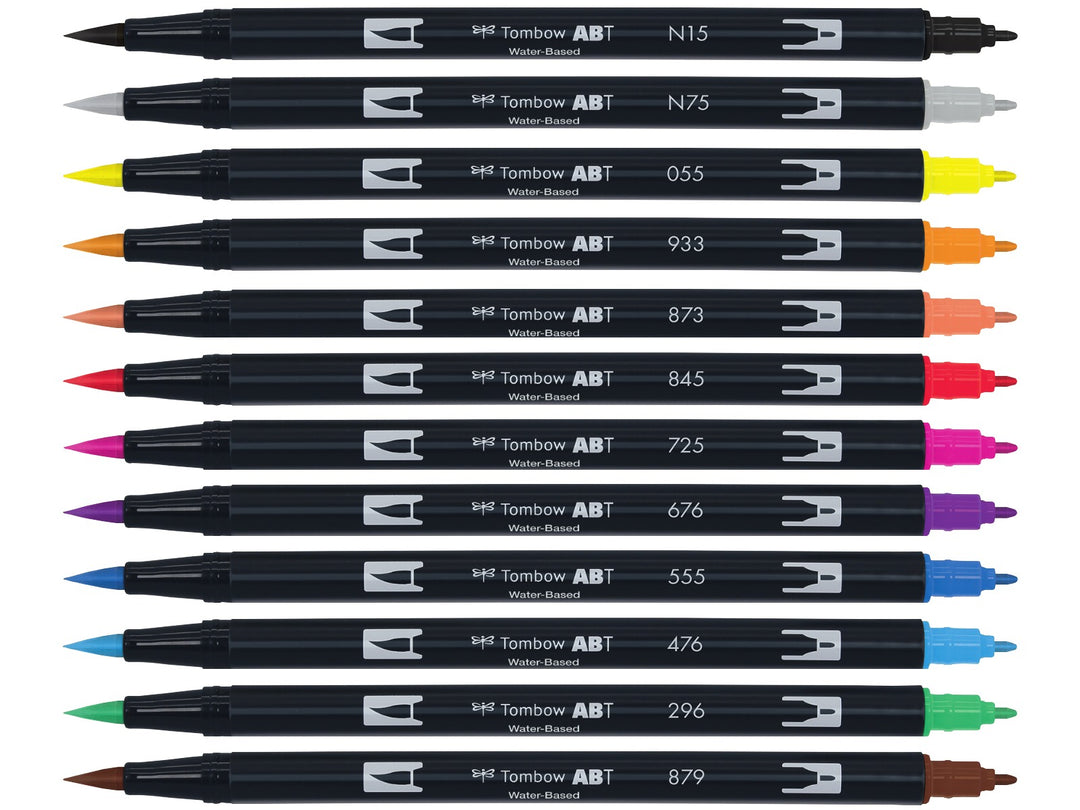 Tombow ABT Dual Brush Pen Primary Colours Set of 12 displayed individually, featuring Black (N15), Cool Grey 3 (N75), Process Yellow (055), Orange (933), Coral (873), Carmine (845), Rhodamine Red (725), Royal Purple (676), Ultramarine (555), Cyan (476), Green (296) and Brown (879), each with dual brush and fine tips visible.