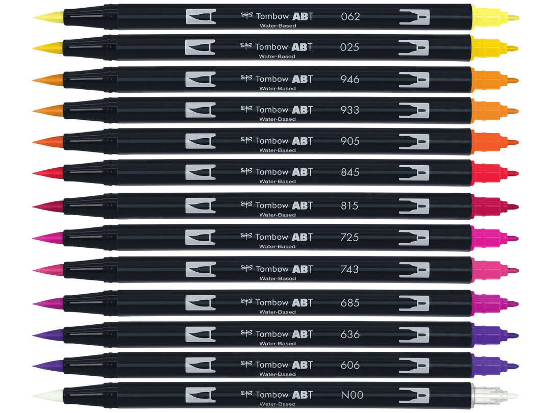 Tombow ABT Dual Brush Pen Sunset Colours Set of 12 displayed individually, featuring Pale Yellow (062), Light Orange (025), Gold Ochre (946), Orange (933), Red (905), Carmine (845), Cherry (815), Rhodamine Red (725), Hot Pink (743), Deep Magenta (685), Imperial Purple (636), Violet (606) and a colourless Blender (N00), each with dual brush and fine tips visible for hand lettering, colouring, illustration and watercolour-style effects.