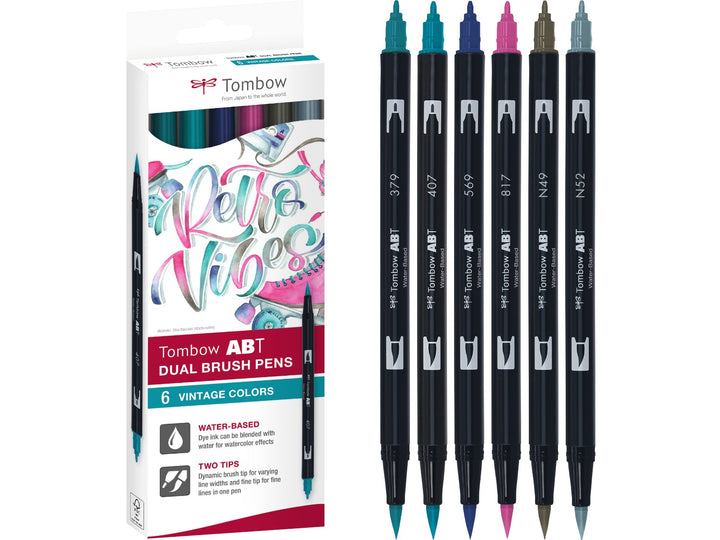 Tombow ABT Dual Brush Pen Vintage Colours Set of 6 featuring Warm Grey 8 (N49), Cool Grey 8 (N52), Jade Green (379), Tiki Teal (407), Jet Blue (569) and Mauve (817), displayed alongside the original retail packaging with dual brush and fine tips for hand lettering, illustration, journaling and creative projects.
