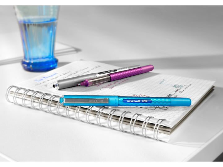 uni-ball Eye Designer UB-157D rollerball pens in Blue, Light Blue and Wine displayed on an open notebook, showcasing visible ink reservoirs, modern designer barrels and smooth liquid Super Ink technology