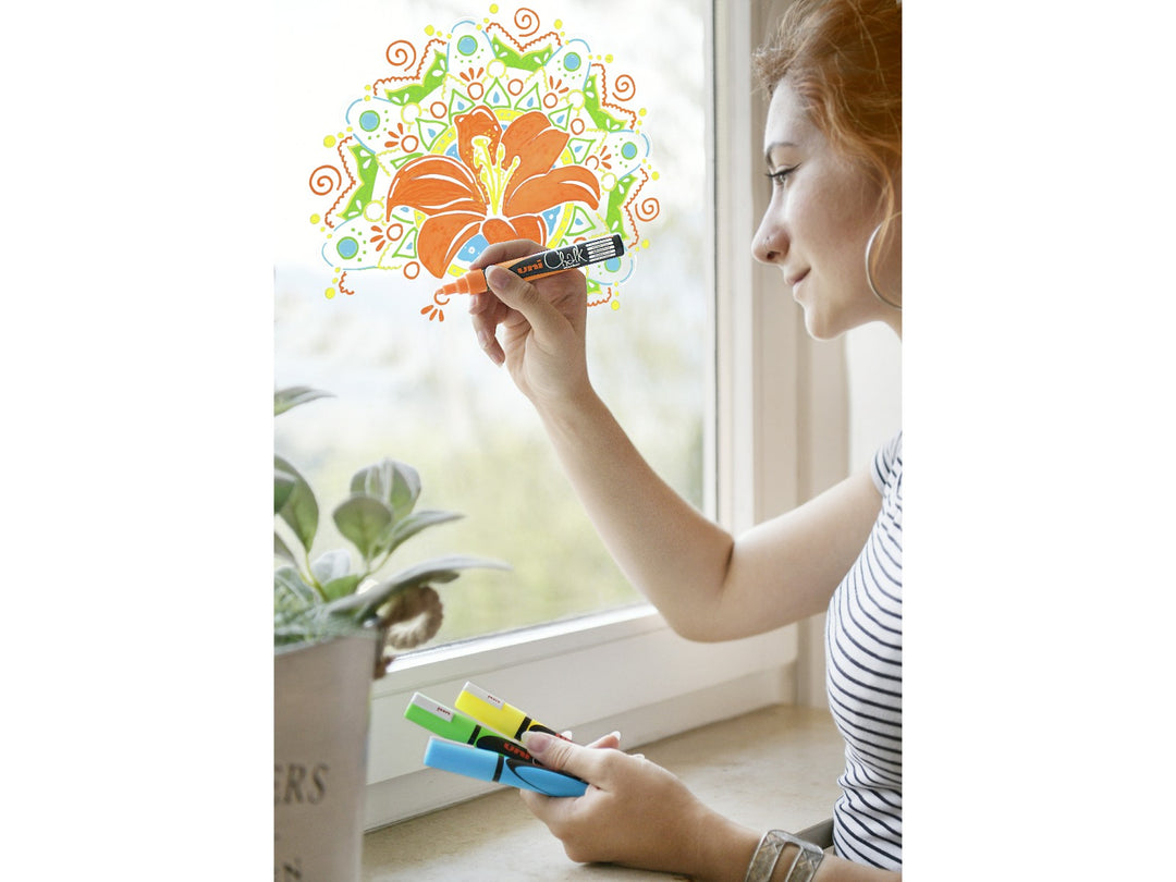 uni ChalkGlass PWE-5M chalk markers being used to create a colourful floral design on a glass window, with orange, green, yellow and light blue markers visible