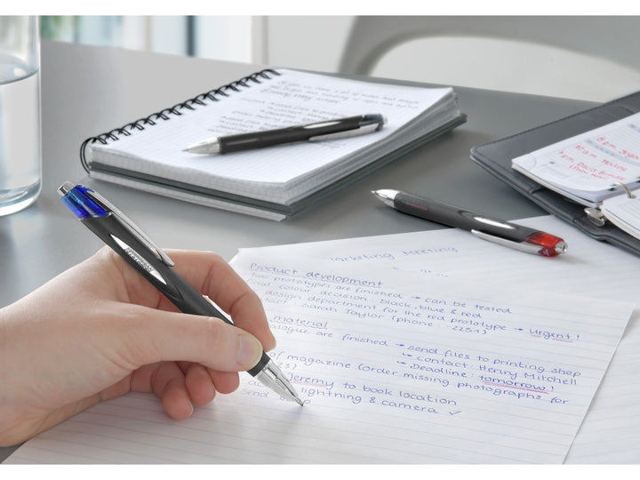 uni Jetstream RT SXN-210 retractable rollerball pens being used for note-taking in an office environment, showcasing smooth Jetstream ink technology, comfortable rubber grips and quick-drying writing performance