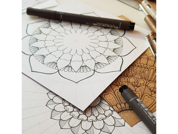 uni PIN Dark Grey fineliners and brush pen displayed alongside detailed mandala-style artwork, showcasing archival-quality dark grey pigment ink for illustration, sketching and creative drawing projects