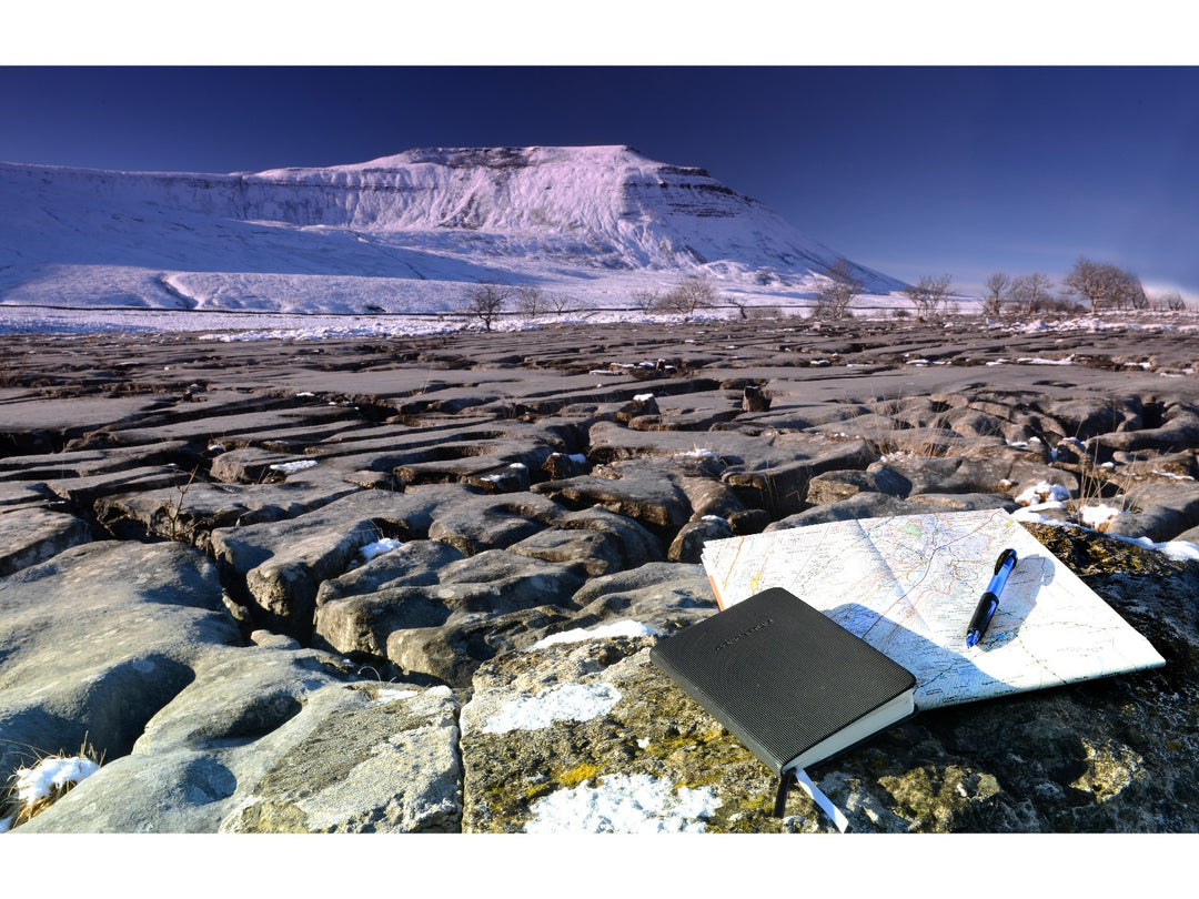 uni Power Tank SN-220 pressurised ballpoint pen resting on a map beside a notebook in a snowy outdoor landscape, demonstrating reliable all-weather writing performance in extreme conditions